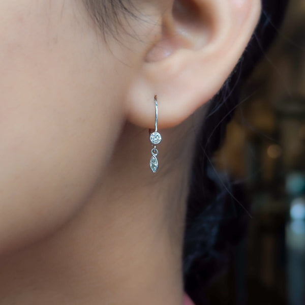 A close-up image of a woman's ear wearing a white gold marquise diamond earring with a dangle design.