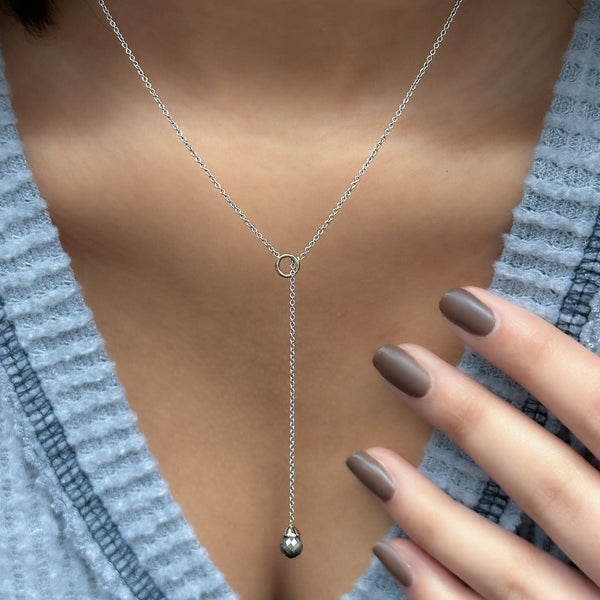 A close-up image of a grey diamond drop necklace with a white gold setting, displayed around a person's neck.