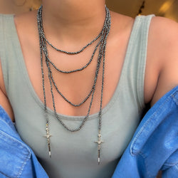 A close-up image of a pyrite beaded necklace with gold diamond daggers, showing a series of round faceted beads and two gold-colored metal pendants.